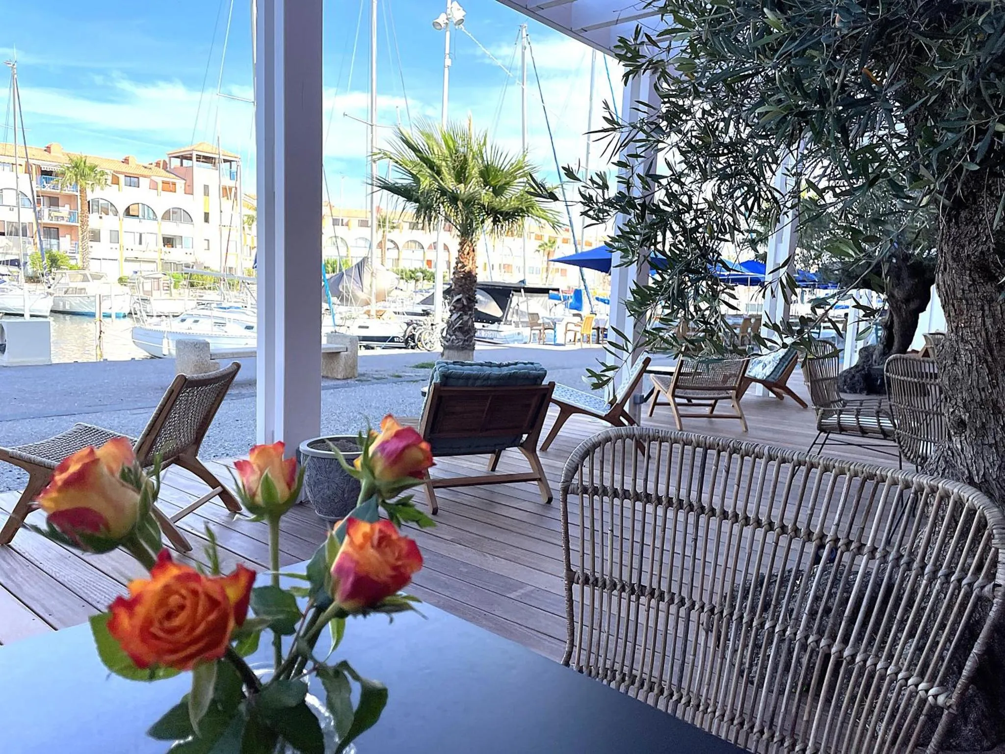 Terrasse ombragée avec mobilier d'extérieur et vue sur un port de plaisance.