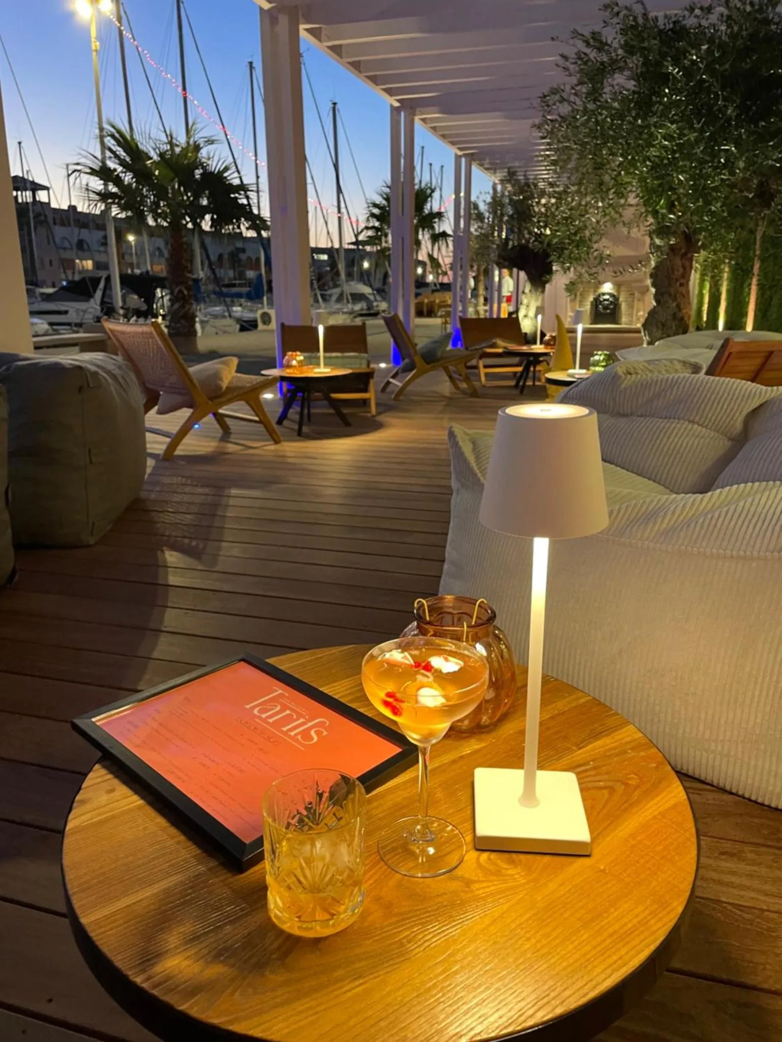 Une table basse avec des boissons et un menu sur une terrasse éclairée.