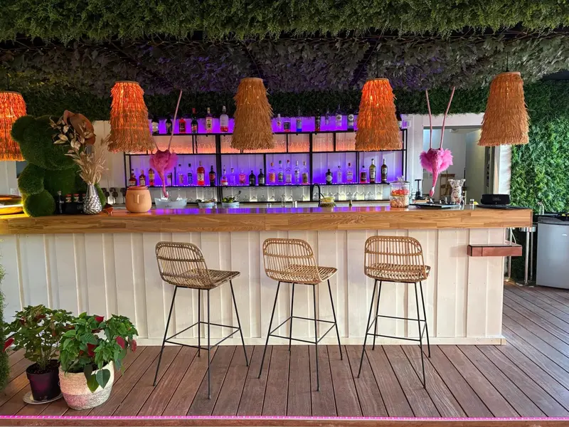 Un comptoir de bar en bois clair avec des tabourets hauts et des suspensions lumineuses.