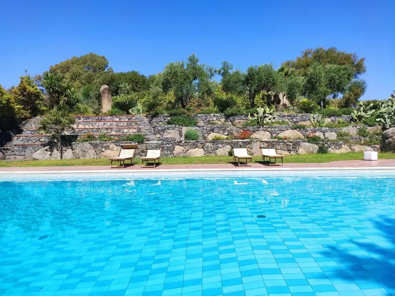 Transats alignés au bord d'une piscine turquoise, avec une végétation luxuriante en arrière-plan.