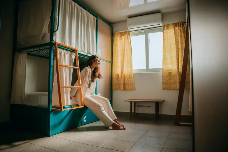 Une femme assise sur un lit superposé dans une chambre lumineuse.