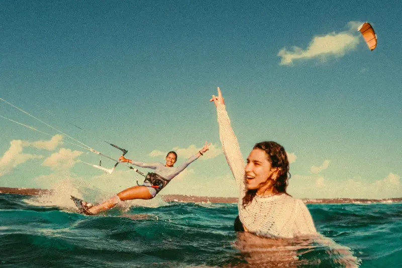 Une femme exulte dans l'eau tandis qu'une autre pratique le kitesurf.