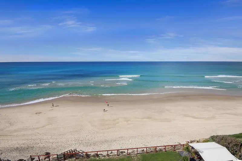 Vue aérienne d'une plage de sable fin bordée par une mer turquoise et une végétation luxuriante.