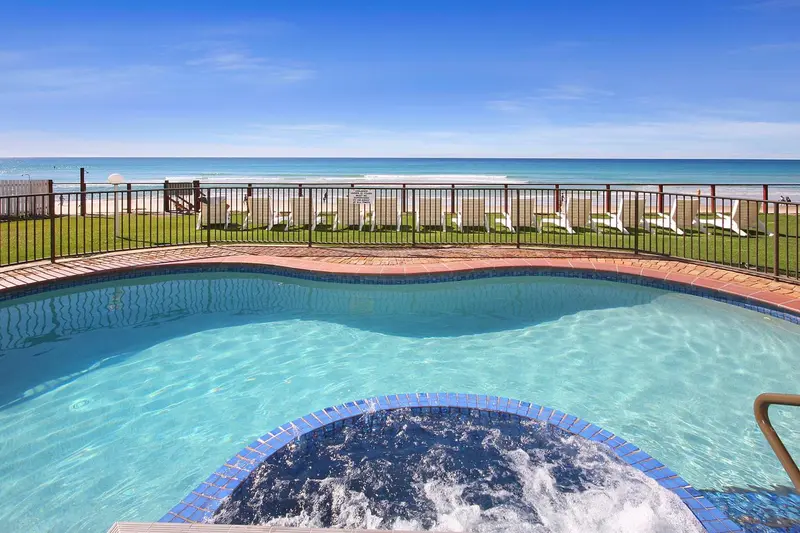 Piscine turquoise avec jacuzzi intégré, vue sur la mer et la plage.
