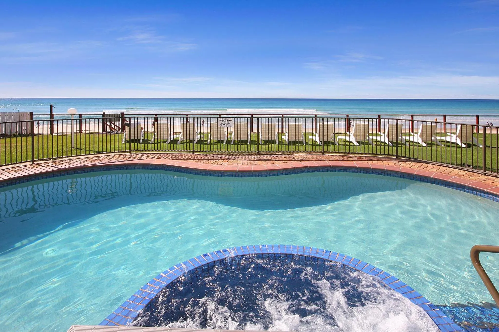 Une piscine avec un jacuzzi intégré offre une vue sur la mer et la plage.