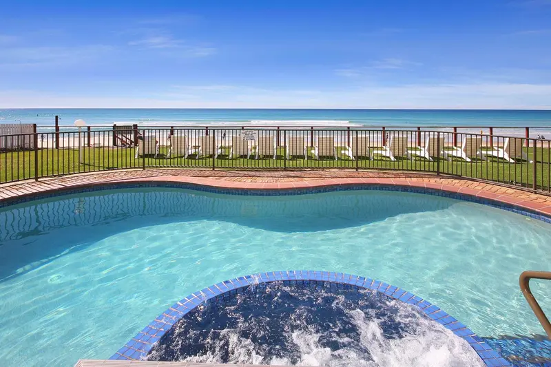Une piscine avec un jacuzzi intégré offre une vue sur la mer et la plage.