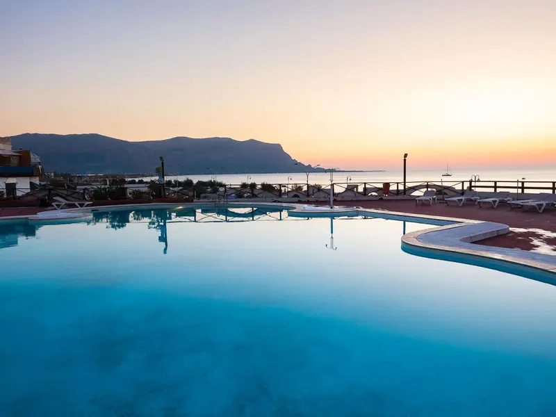 Une piscine au bord de la mer avec une vue sur les montagnes au coucher du soleil.