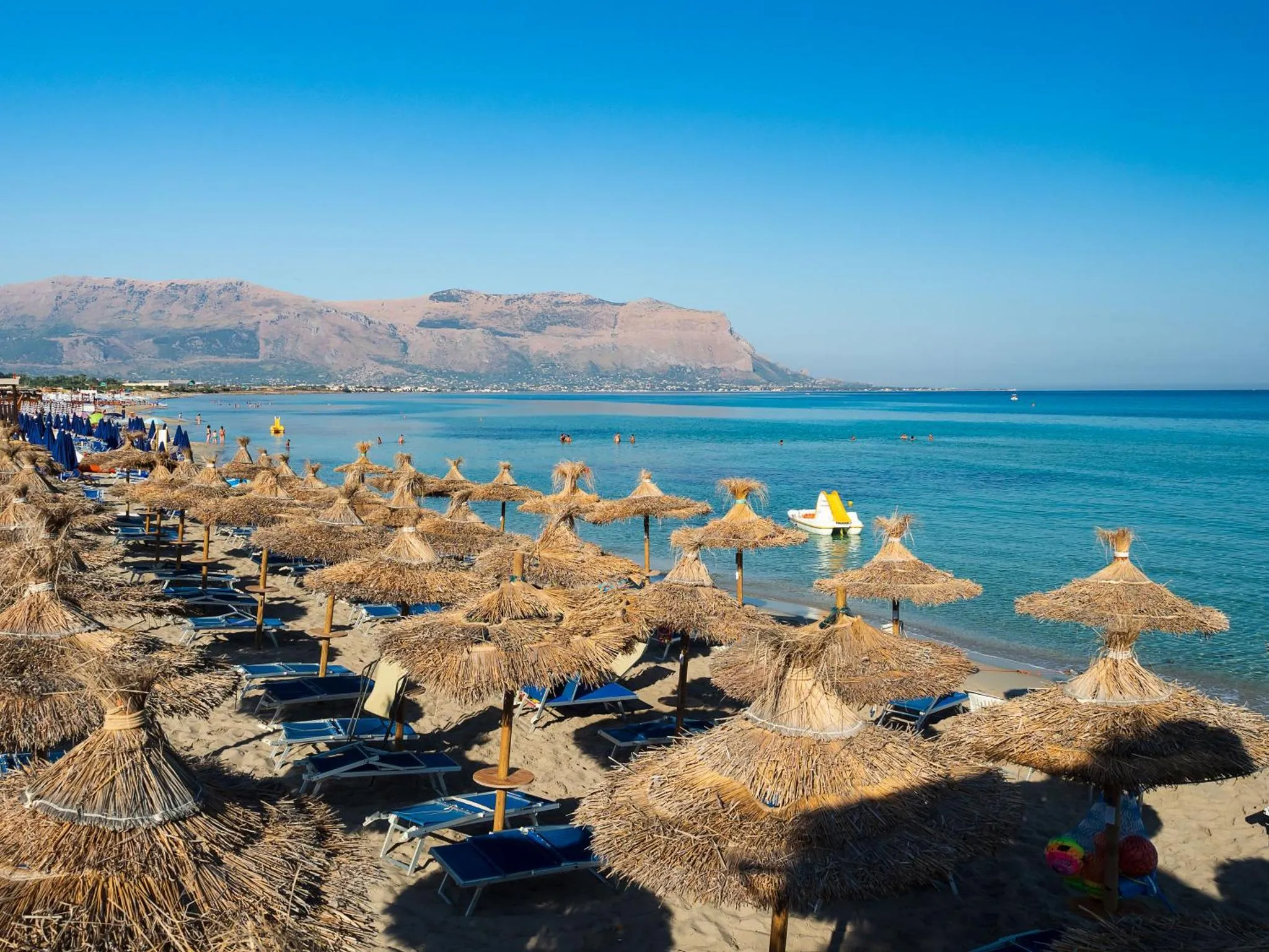 Plage de sable avec parasols de paille et transats face à la mer.