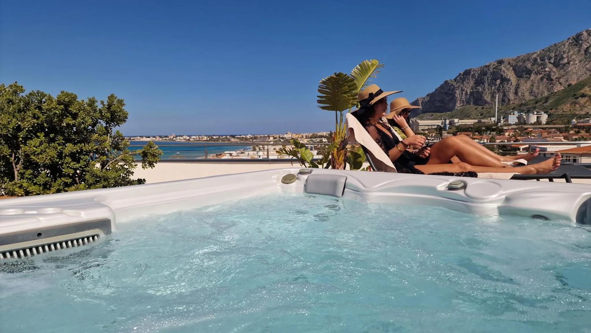 Deux personnes se détendent dans un jacuzzi avec vue sur la mer et les montagnes.