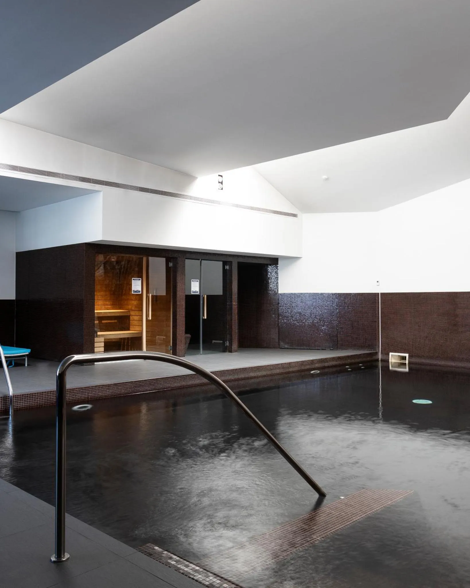Une piscine intérieure sombre avec un sauna visible au fond.