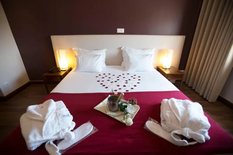 Une chambre avec un grand lit recouvert d'une courtepointe rouge et de pétales de fleurs.