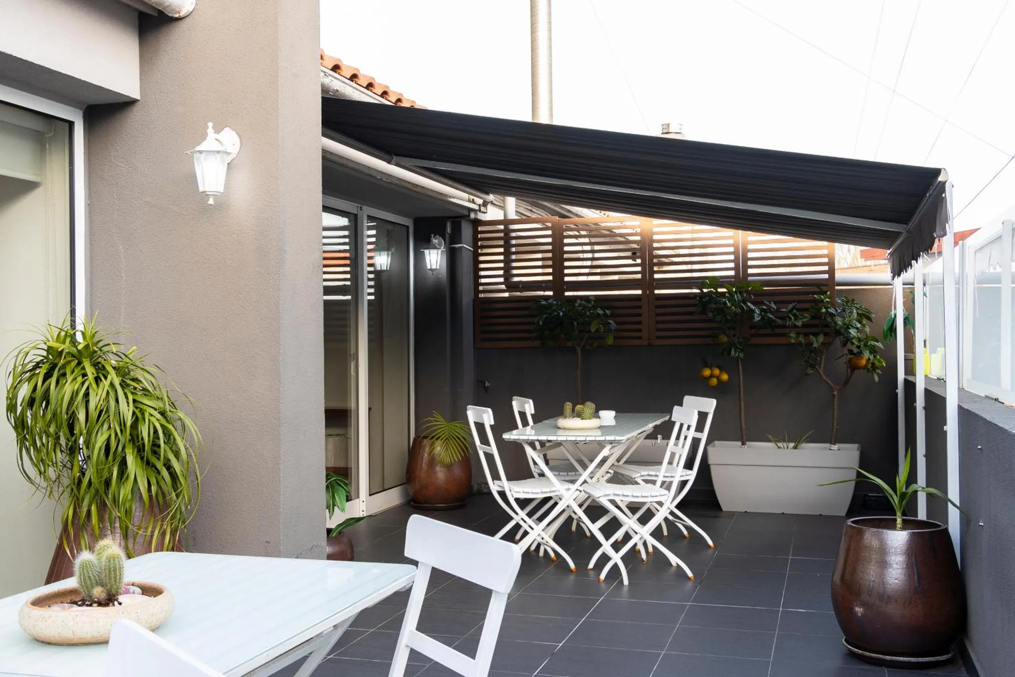 Une table et des chaises blanches sont disposées sur une terrasse ombragée.