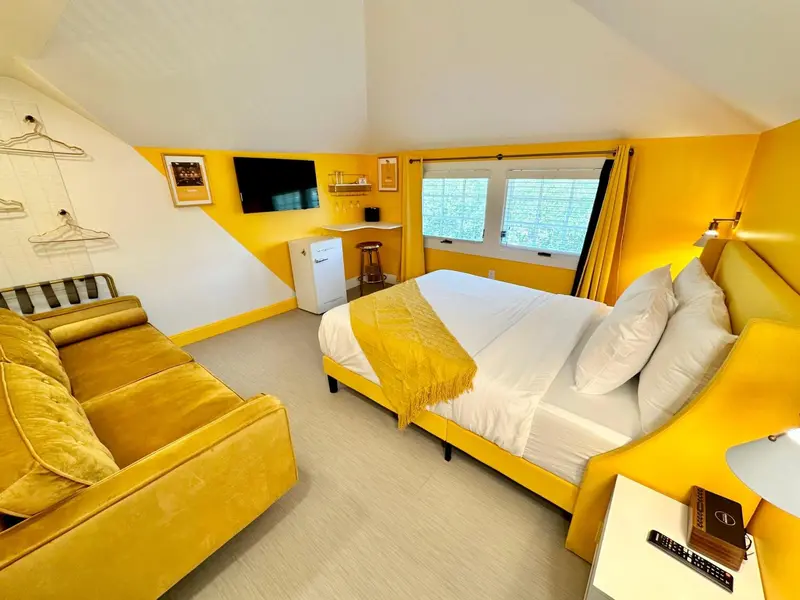 Une chambre jaune vif avec un canapé, un lit et une télévision murale.