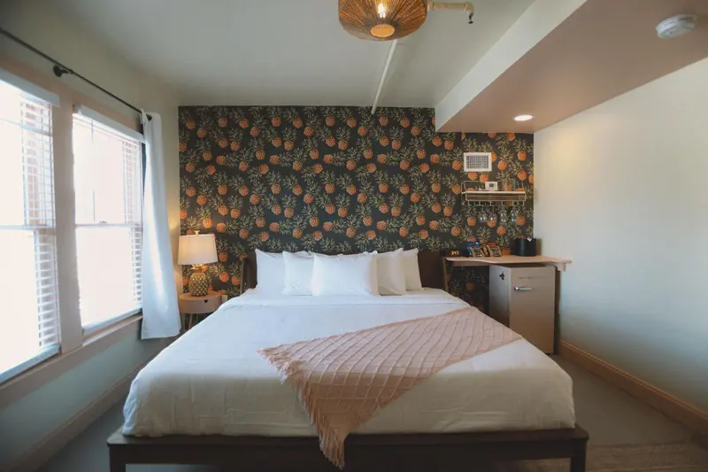 Une chambre lumineuse avec un lit recouvert d'une couverture rose et un mur décoré de motifs tropicaux.