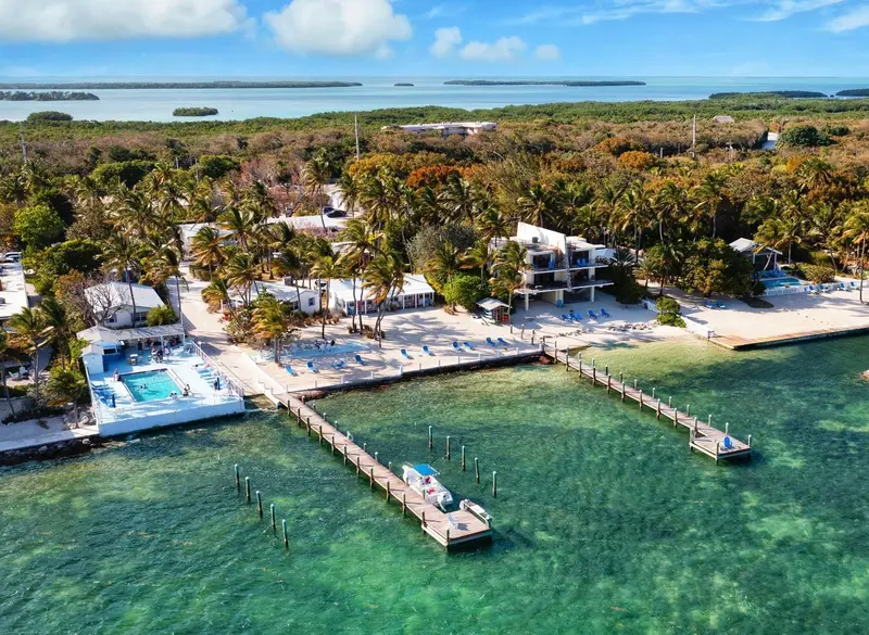 Vue aérienne d'un complexe hôtelier avec piscine, pontons et plage.