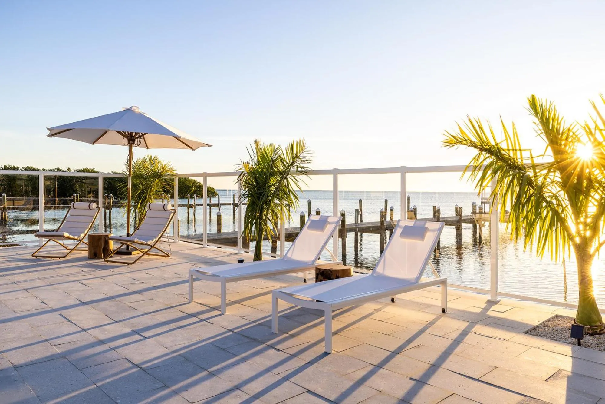 Transats blancs disposés sur une terrasse ensoleillée face à la mer.