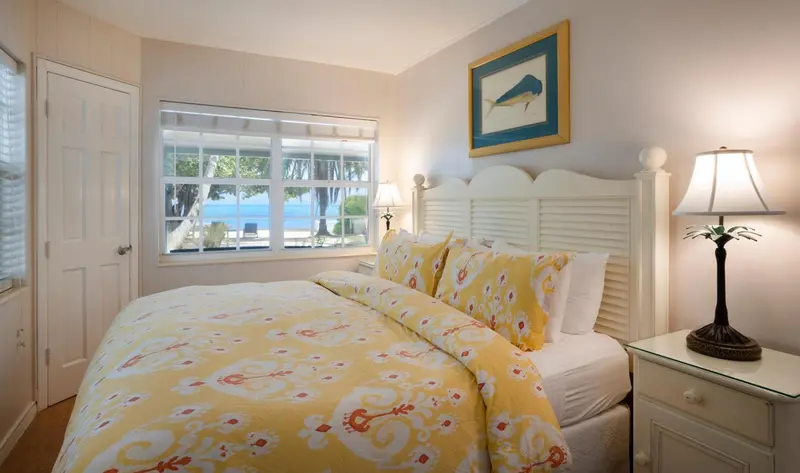 Une chambre lumineuse avec un lit recouvert d'une couette fleurie et une vue sur la mer.