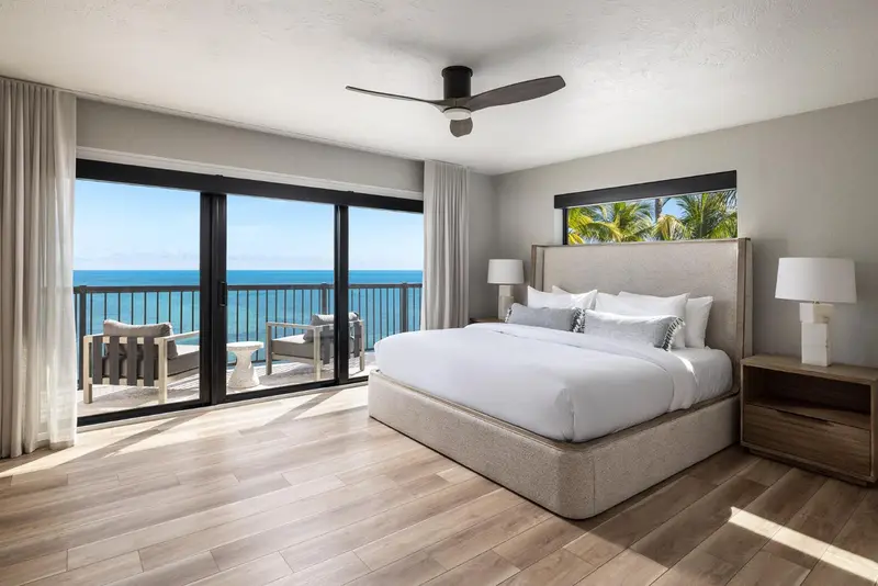 Une chambre lumineuse avec un grand lit et une vue sur la mer depuis un balcon.