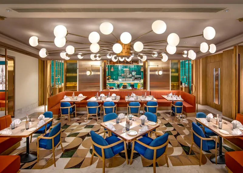 Une salle de restaurant lumineuse avec des tables dressées et des banquettes colorées.