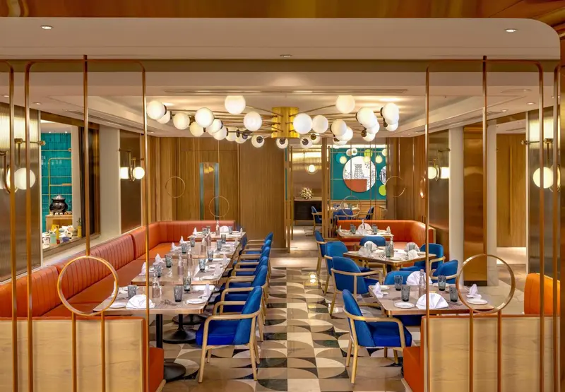 Une salle de restaurant lumineuse avec des tables dressées et des banquettes colorées.