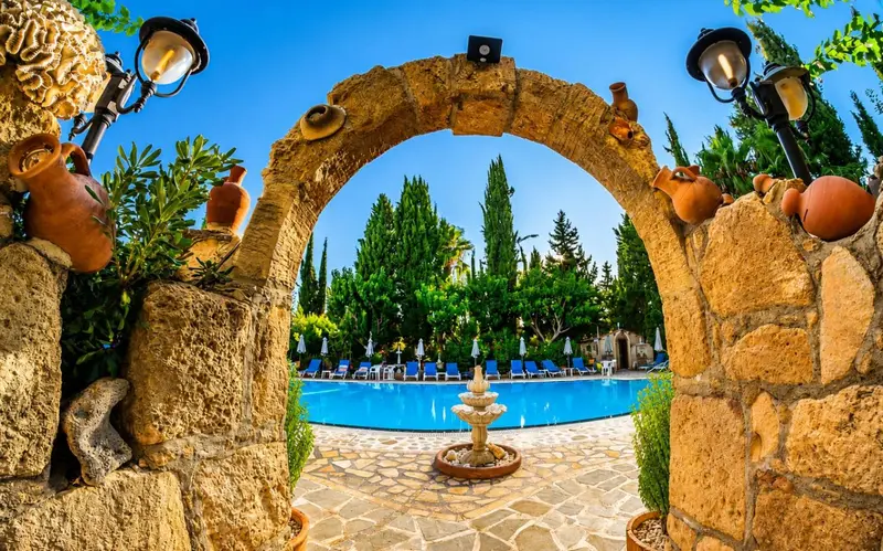 Une arche en pierre donne sur une piscine turquoise entourée de végétation luxuriante.