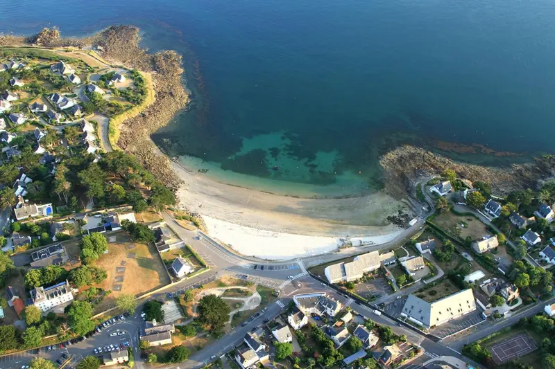 Vue aérienne d'une plage de sable fin bordée de bâtiments et de végétation.