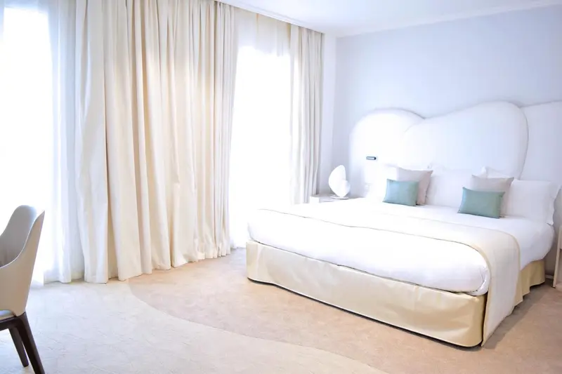 Une chambre lumineuse avec un grand lit et des rideaux clairs.