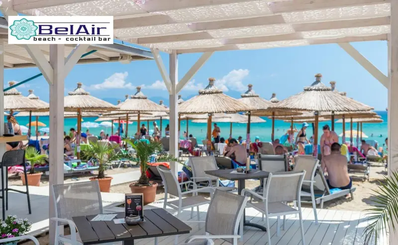 Terrasse ombragée avec tables et chaises sur une plage ensoleillée.