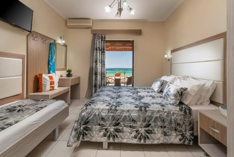 Une chambre lumineuse avec un grand lit et un accès à un balcon donnant sur la mer.