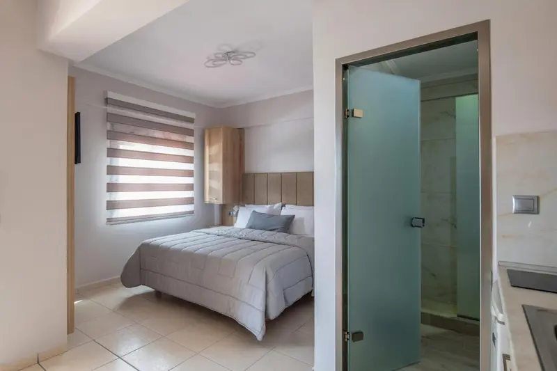 Une chambre lumineuse avec un lit double et une salle de bain visible à travers une porte vitrée.