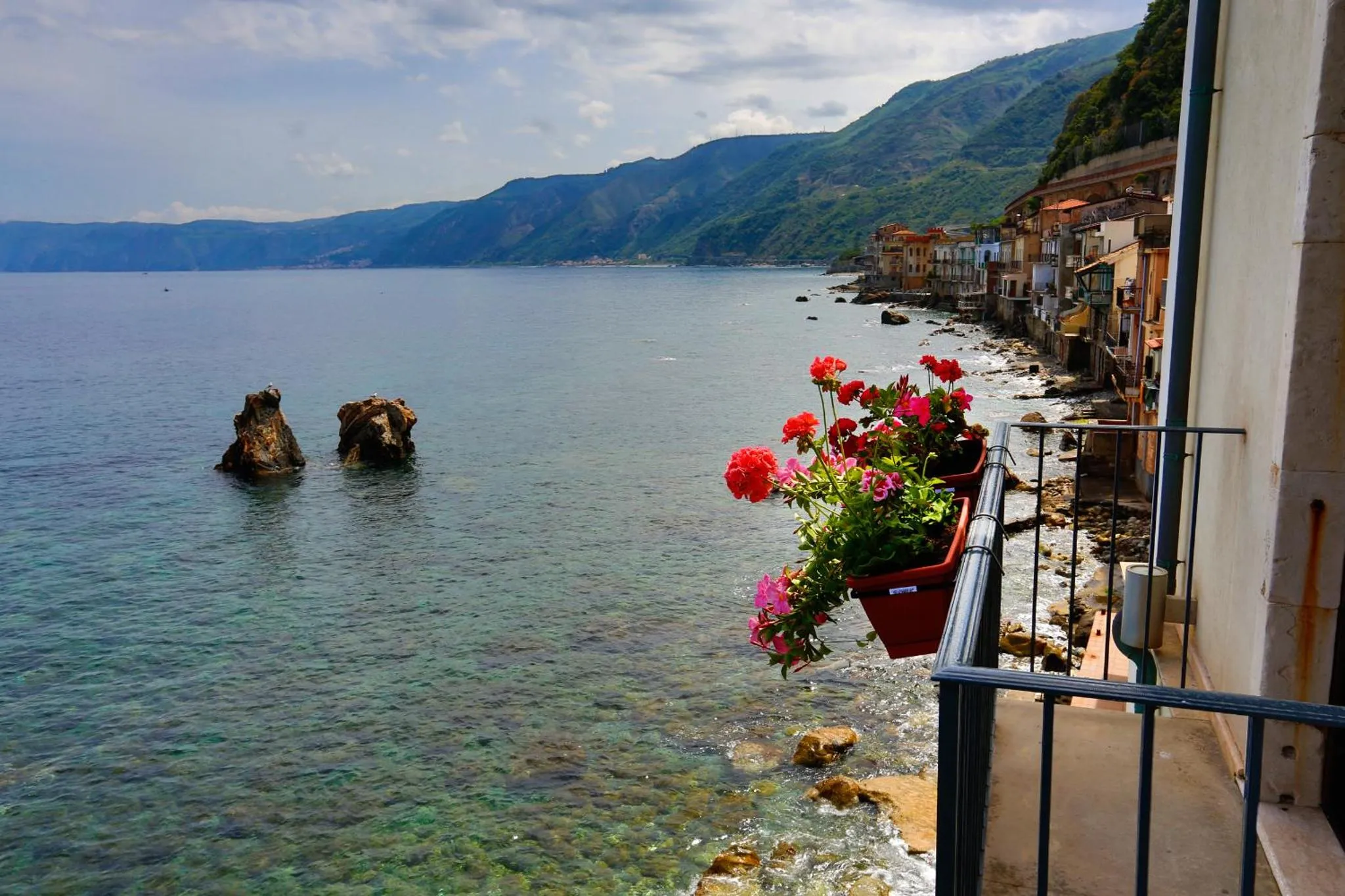 Vue sur la mer depuis un balcon fleuri avec des rochers en contrebas.