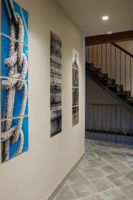 Des tableaux abstraits ornent un mur le long d'un couloir avec un escalier.