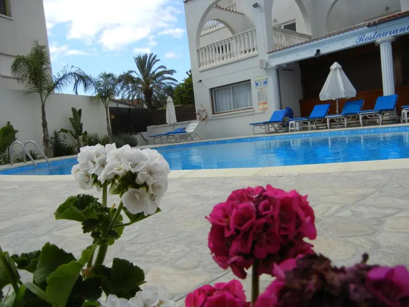 Une piscine turquoise bordée de fleurs et de chaises longues bleues.