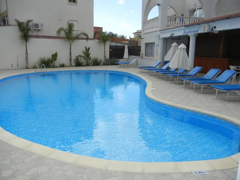 Une piscine bleue entourée de transats blancs sous le soleil.