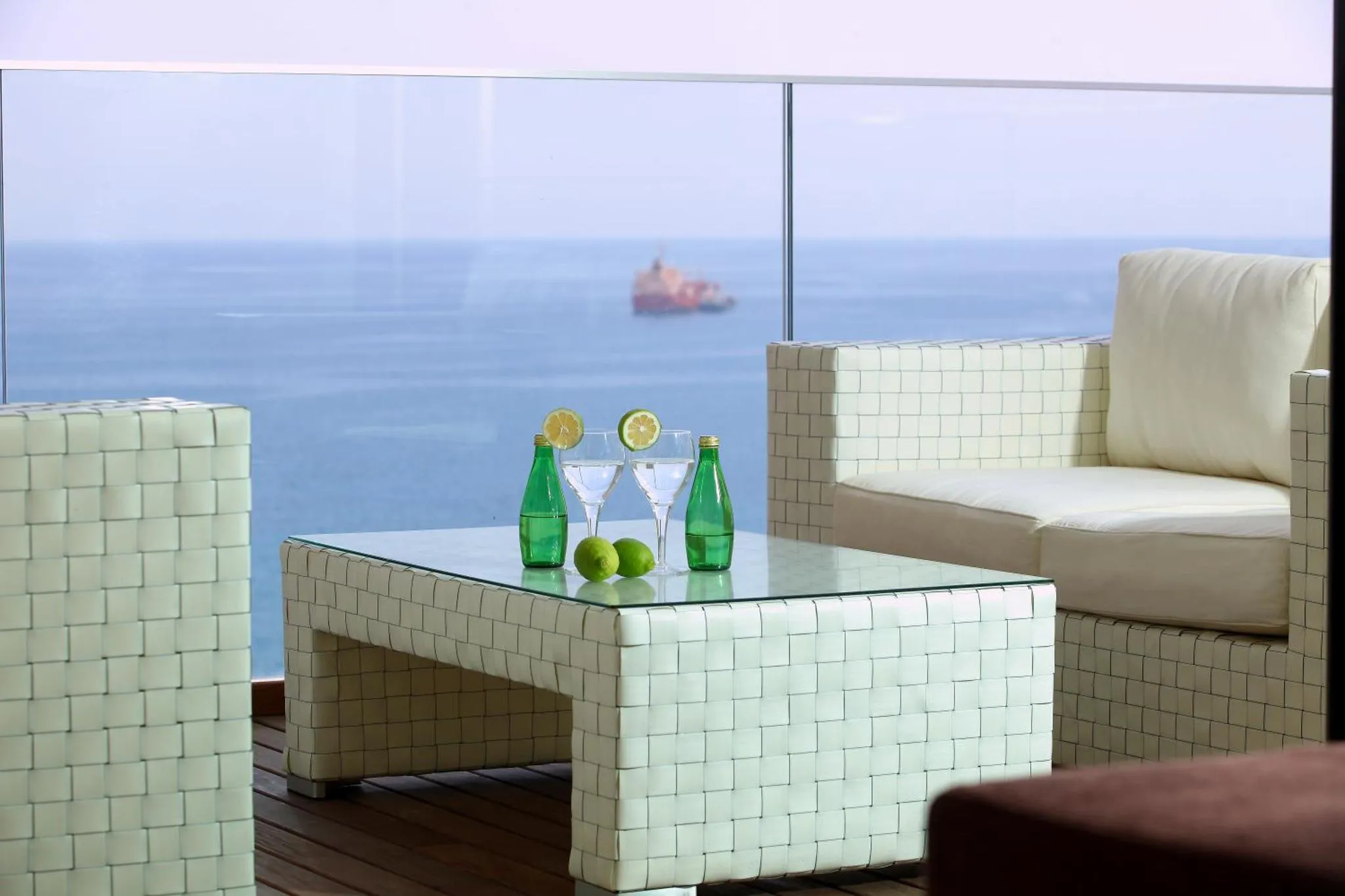 Une table basse en osier avec des boissons fraîches sur une terrasse ensoleillée avec vue sur la mer.