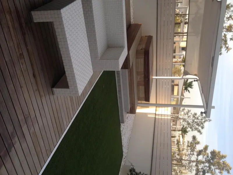 Terrasse en bois avec assises en mosaïque et gazon synthétique.