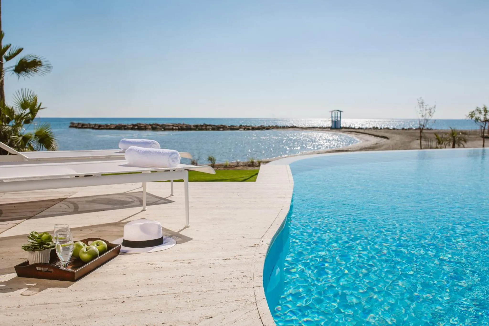 Transats blancs au bord d'une piscine à débordement avec vue sur la mer.