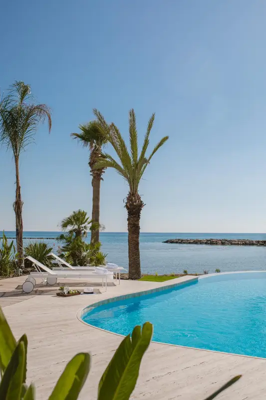 Transats blancs alignés au bord d'une piscine turquoise face à la mer.