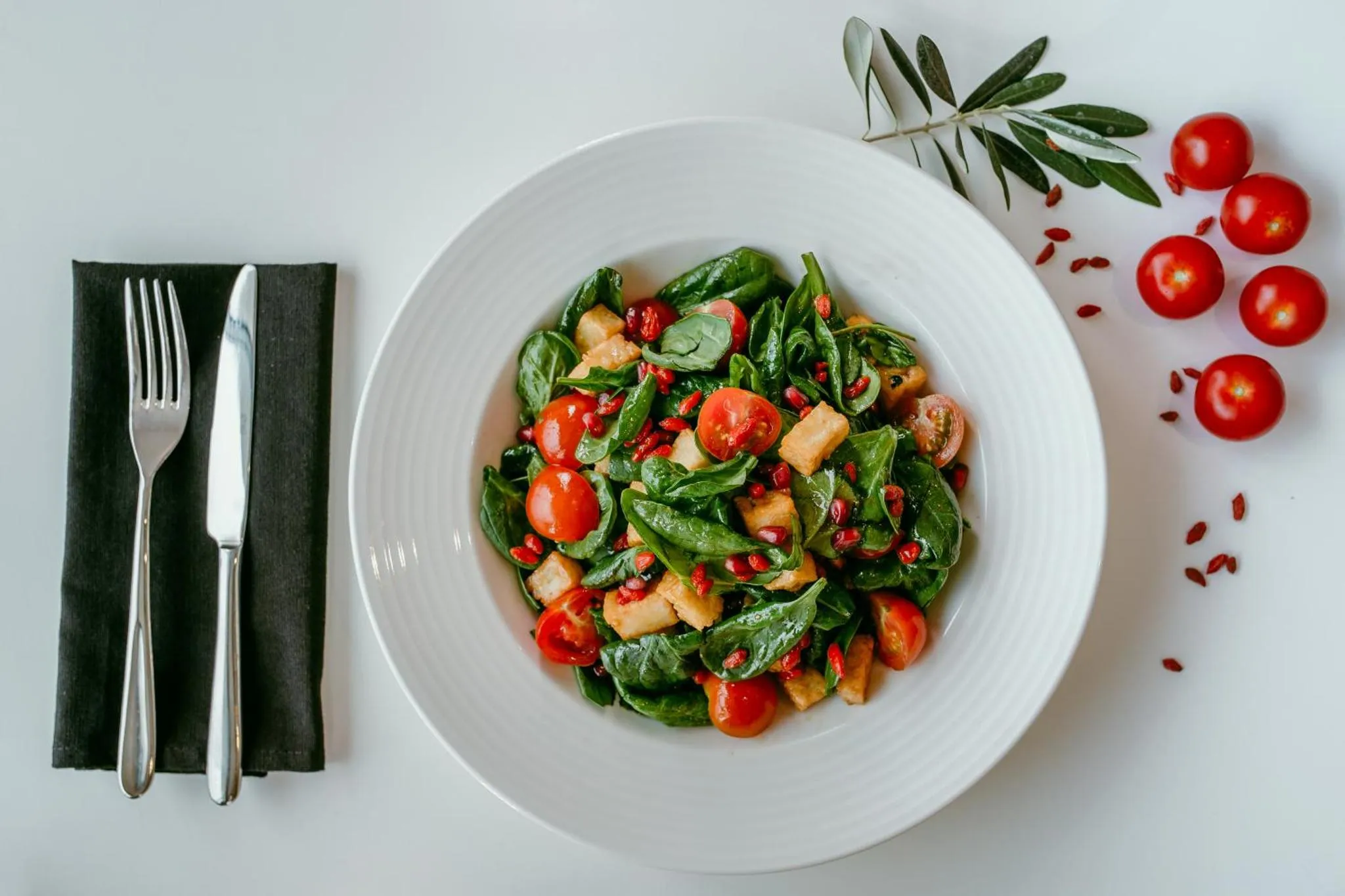 Salade colorée avec des tomates cerises et des feuilles vertes, présentée sur une assiette blanche.