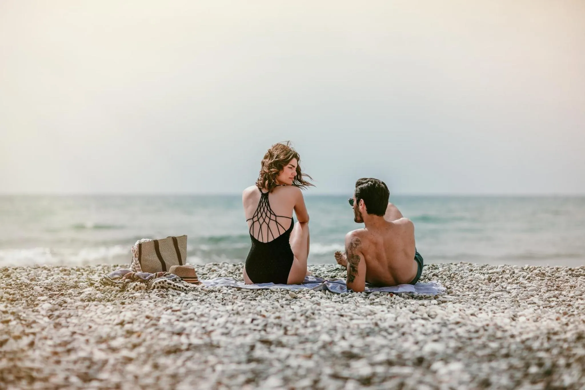 Un couple se détend sur une plage de galets face à la mer.