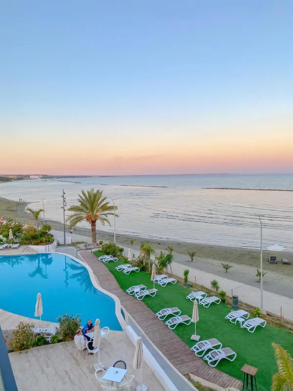 Transats alignés au bord d'une piscine face à la mer au coucher du soleil.