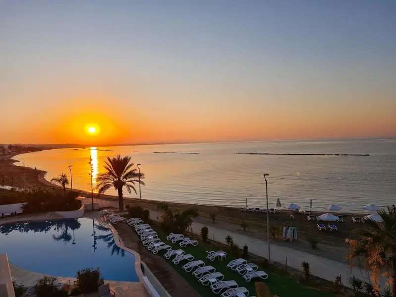 Coucher de soleil sur la mer depuis une terrasse avec piscine et transats.