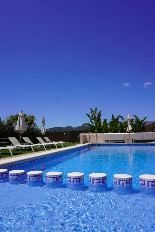 Une piscine bleue avec des marches et des transats blancs sous le soleil.