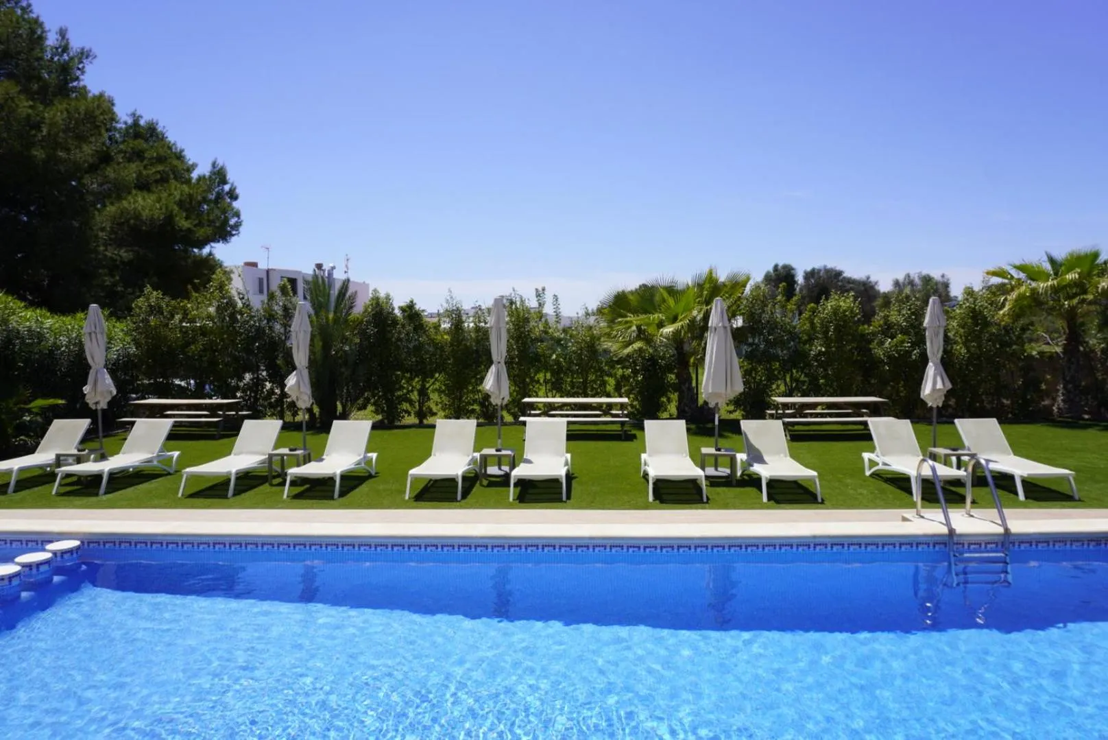 Transats blancs alignés au bord d'une piscine bleue en extérieur.