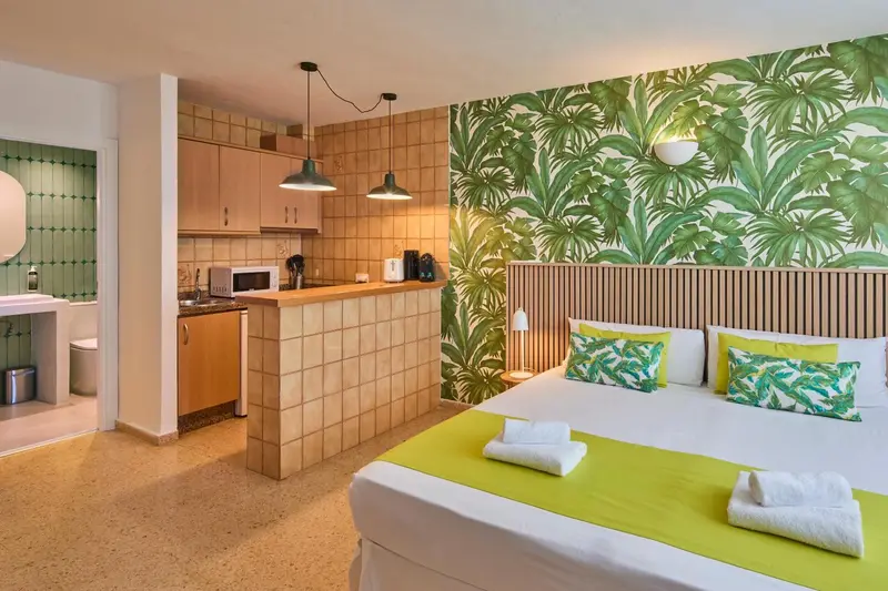 Une chambre lumineuse avec un espace cuisine et un lit recouvert d'une couverture verte.