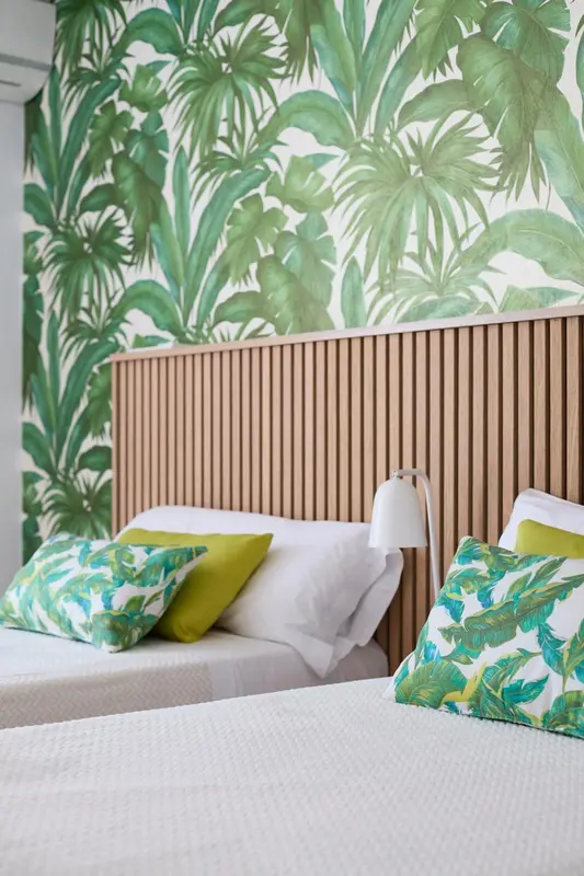 Une chambre avec deux lits simples et un mur décoré de motifs tropicaux.