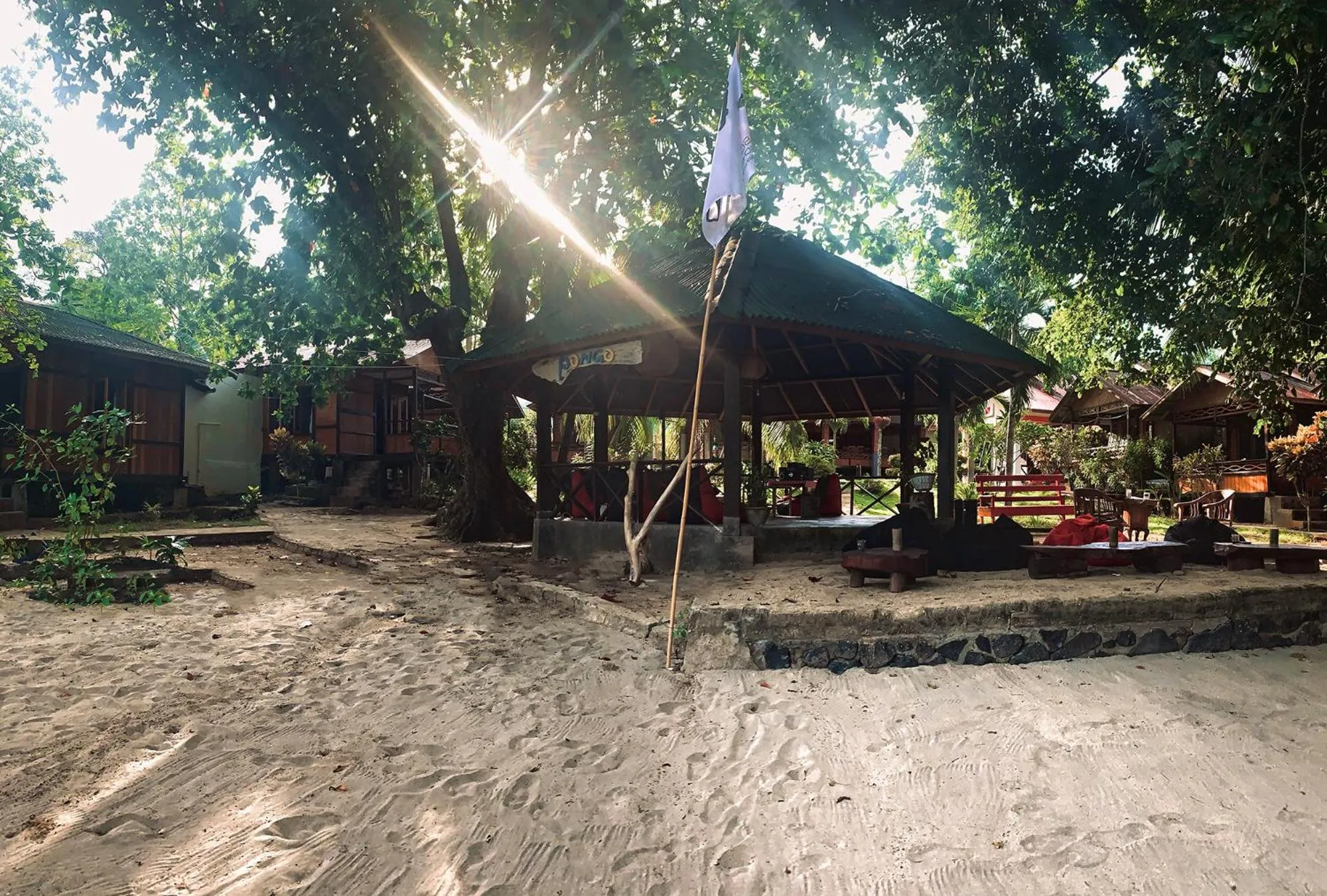 Un espace de détente ombragé s'ouvre sur une plage de sable clair.