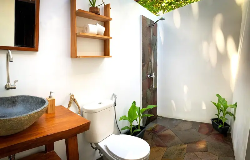 Une salle de bain ouverte avec douche à l'italienne et lavabo en pierre.