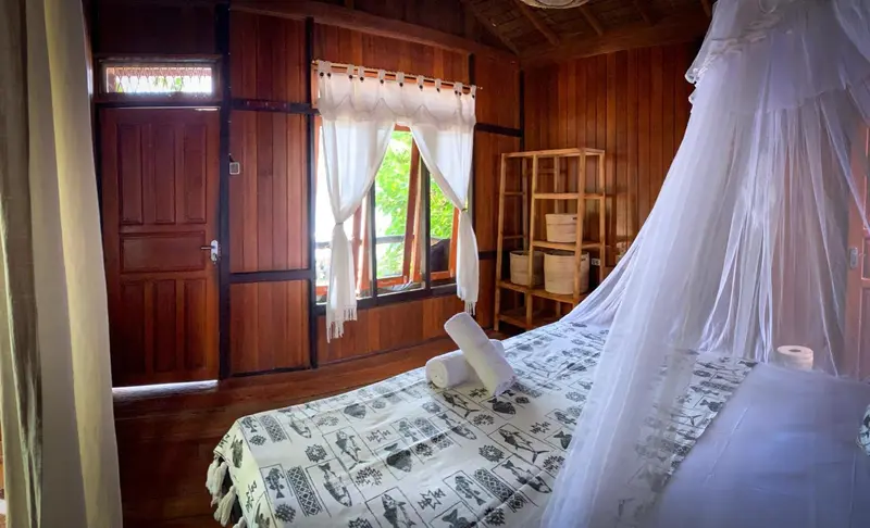 Une chambre lumineuse avec un lit recouvert d'une moustiquaire et un mobilier en bois.