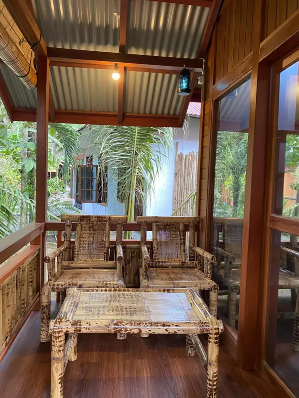 Terrasse en bois avec mobilier en rotin et végétation luxuriante en arrière-plan.